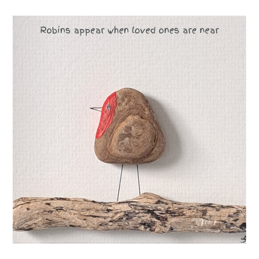 Decorative stone with natural wing markings and a red painted breast, placed on a white surface with text and a piece of driftwood.