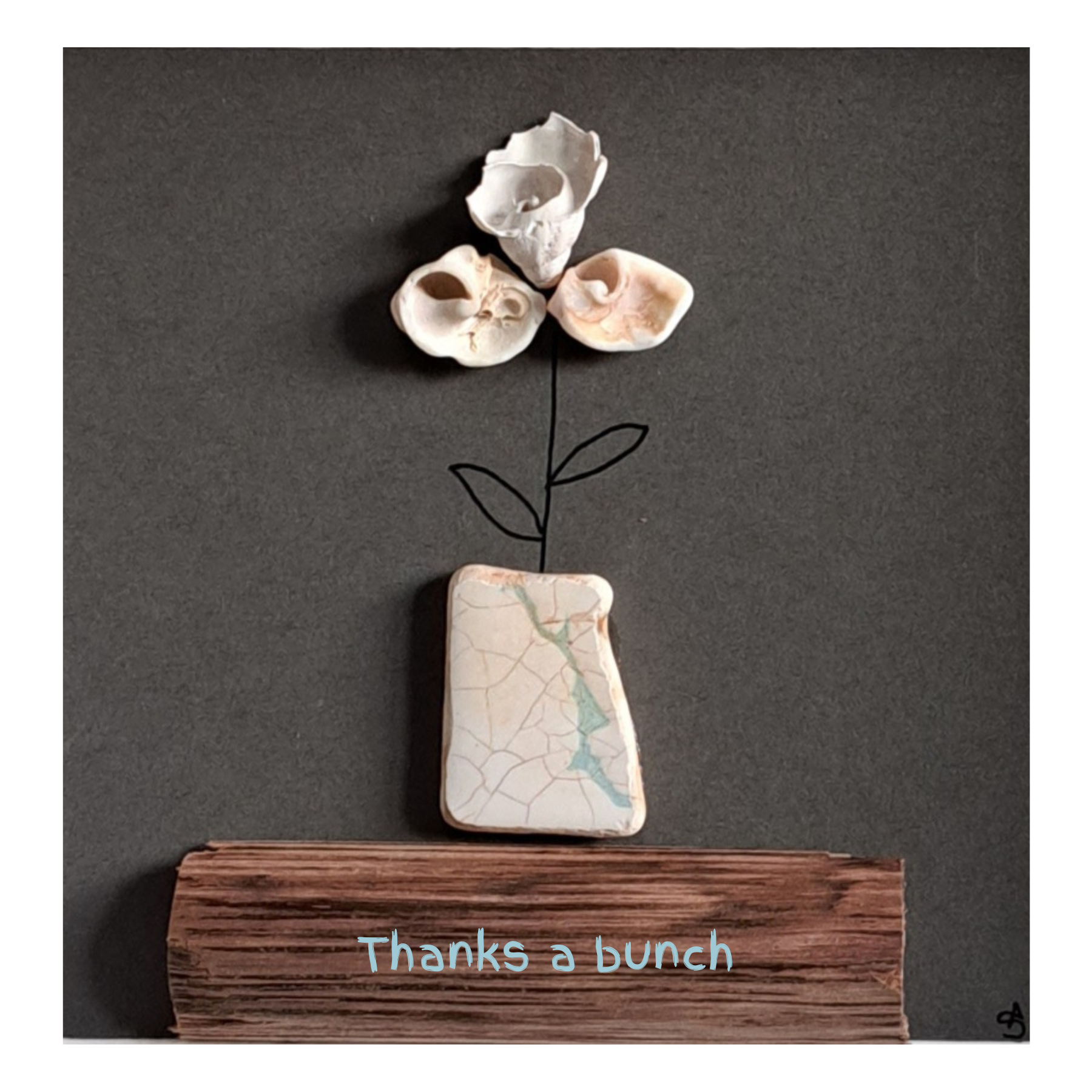 Decorative shell flowers, ceramic vase and wooden block with 'Thanks a bunch' text on a dark background